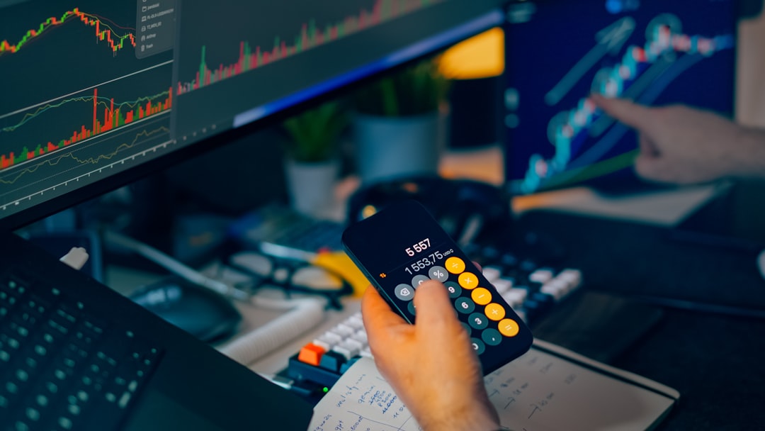 Financial trading workstation stock crypto investment analysis. Closeup hand holding smartphone calculator desk monitors charts candlesticks graphs market data savings portfolio planning risk management economy finance technology office night lighting focus strategy performance growth profit volatility currency bitcoin ethereum exchange dashboard indicators keyboard notebook calculations